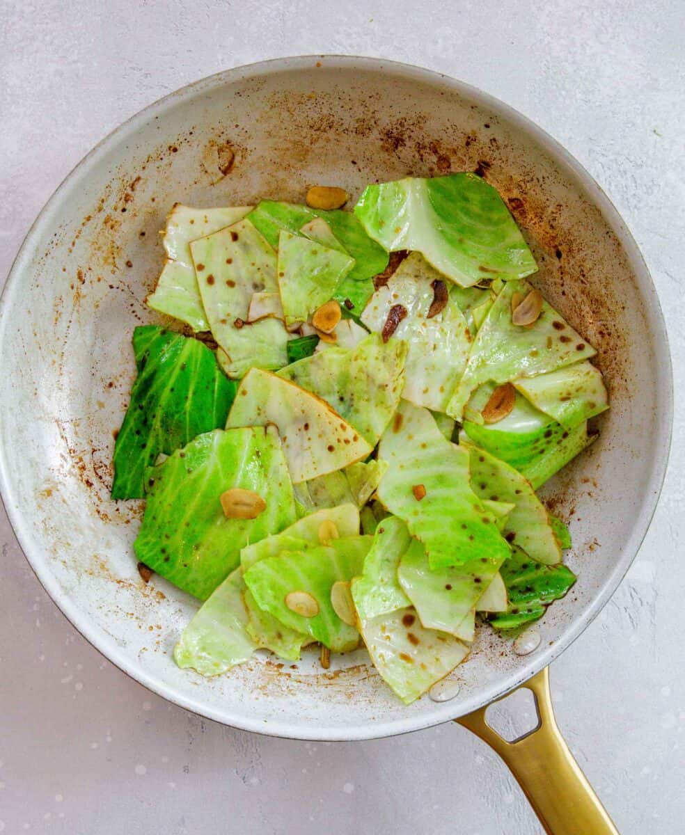 cabbage being sautéd in a skillet with sliced garlic and soy sauce