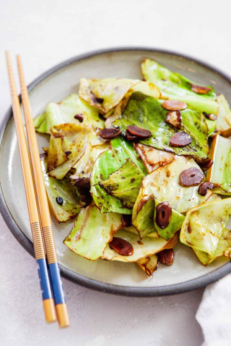 stir fry cabbage tossed in soy sauce with garlic slices on a plate with wooden chopsticks laying on top of the plate