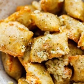 up close image of baked pizza rolls in a ceramic bowl with generous amount of grated parmesan, italian seasoning, and fresh garlic on top