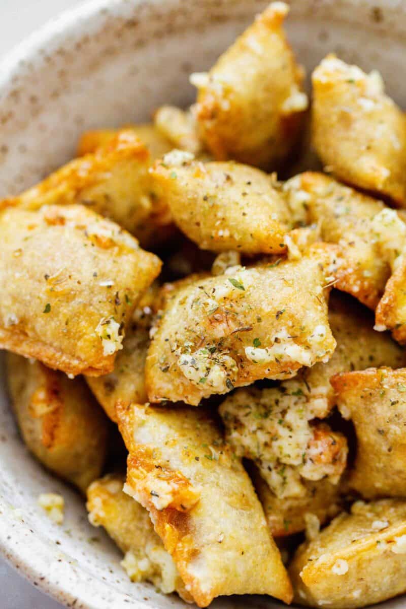 up close image of baked pizza rolls in a ceramic bowl with generous amount of grated parmesan, italian seasoning, and fresh garlic on top