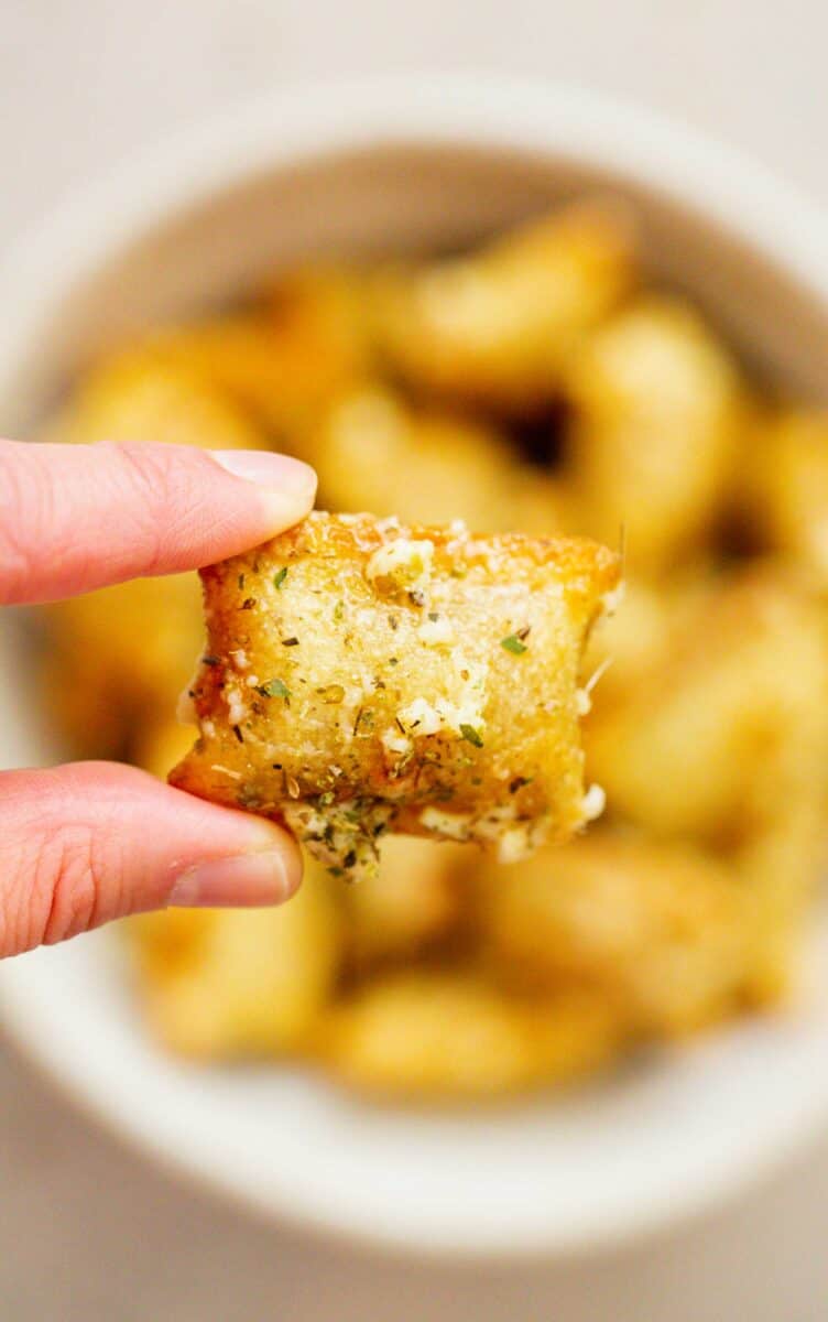 a pointer finger and thumb hold a baked pizza roll covered with grated parmesan, garlic, and italian seasoning