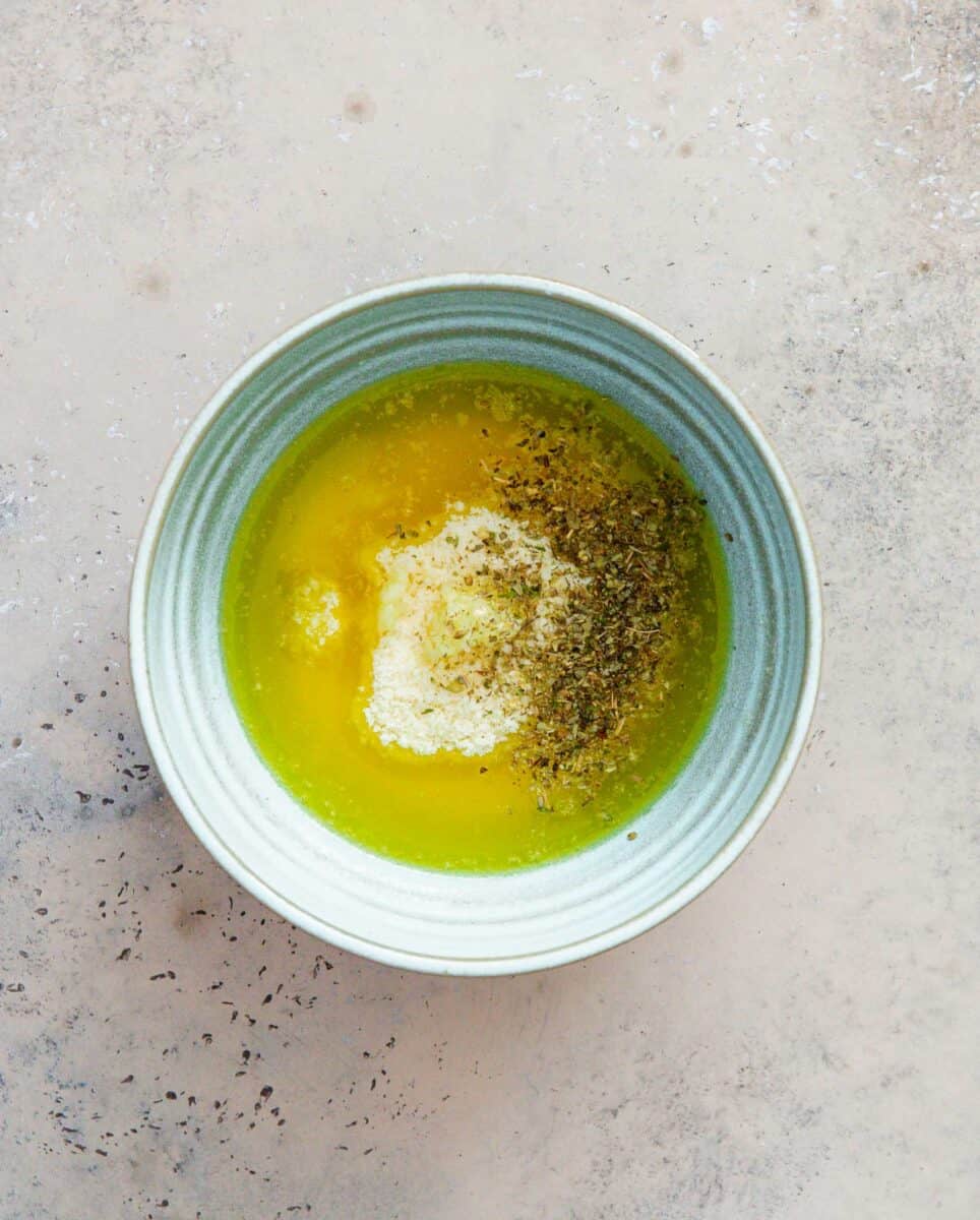 melted butter, parmesan cheese, minced garlic, and Italian seasoning in a light blue ceramic bowl