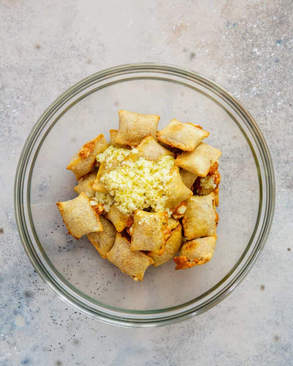 butter garlic mixture on top of the baked pizza rolls in a large clear bowl