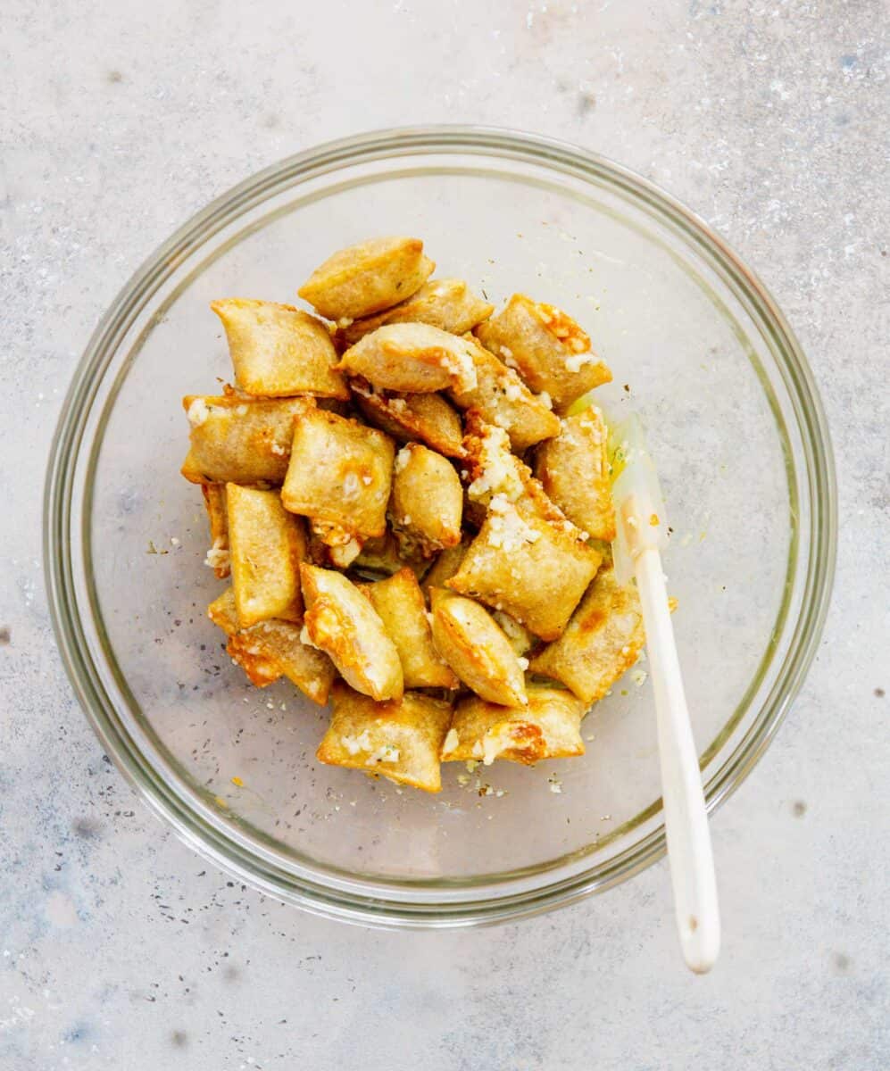 a spatula is in a large clear bowl with the baked pizza rolls and butter garlic mixture