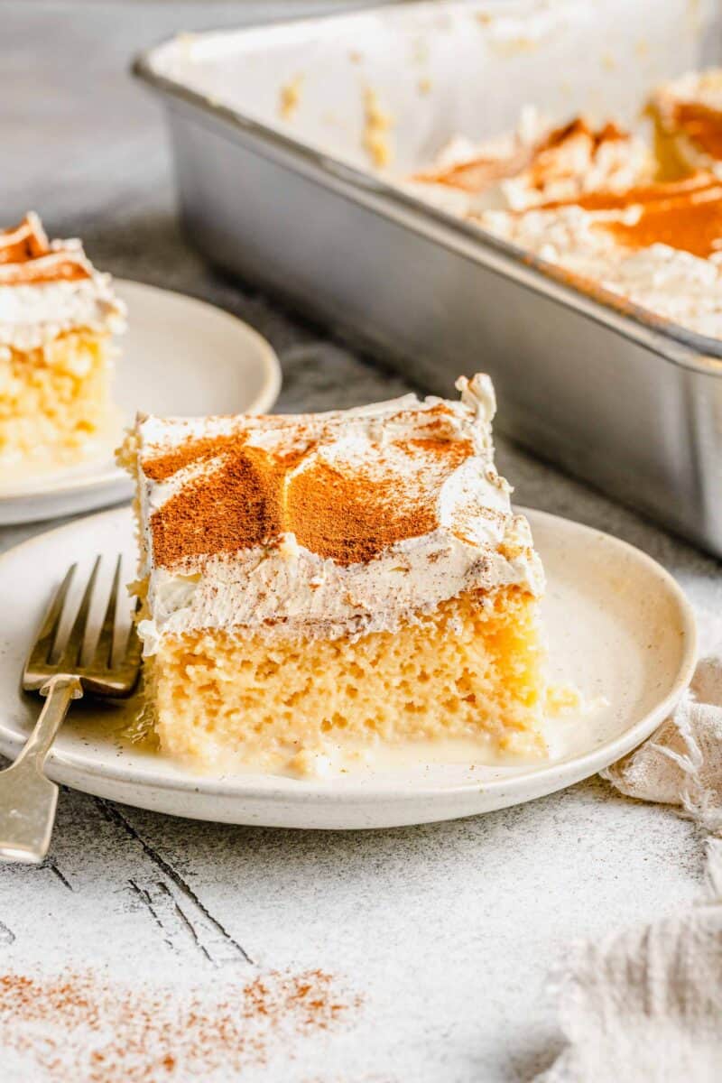 2 slices of tres leches cake on plates with a fork next to the cake pan.