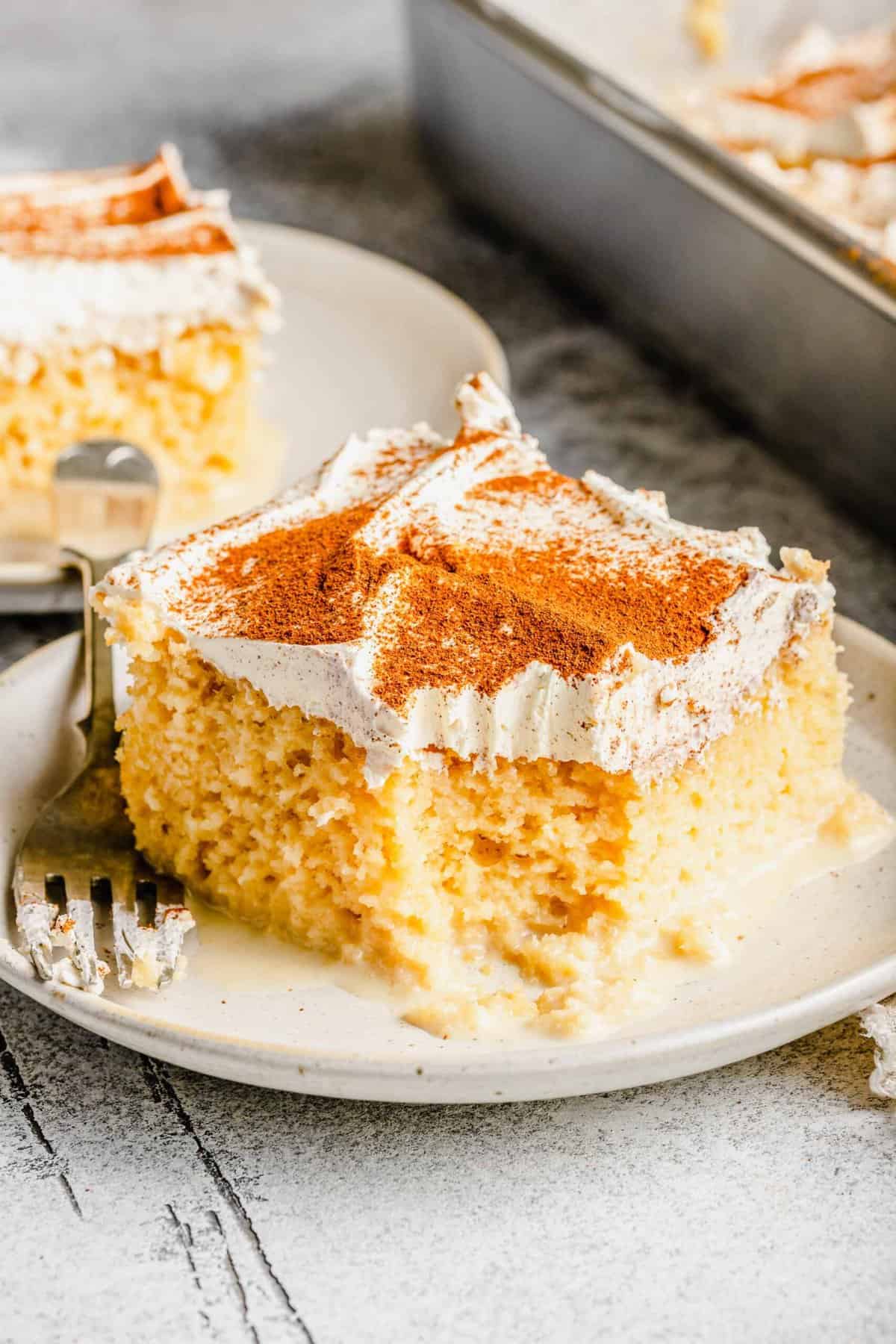 2 slices of tres leches cake on plates with a fork next to the cake pan.