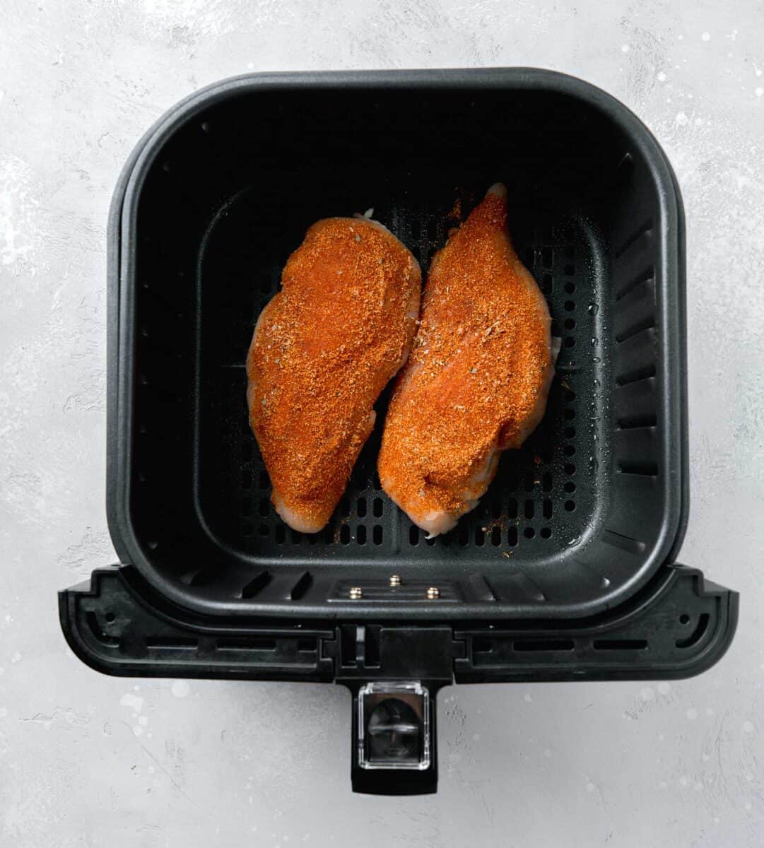 raw chicken coated in blackening seasoning inside the air fryer basket