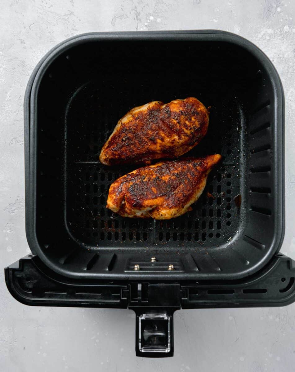 cooked blackened chicken breasts in the basket of an air fryer