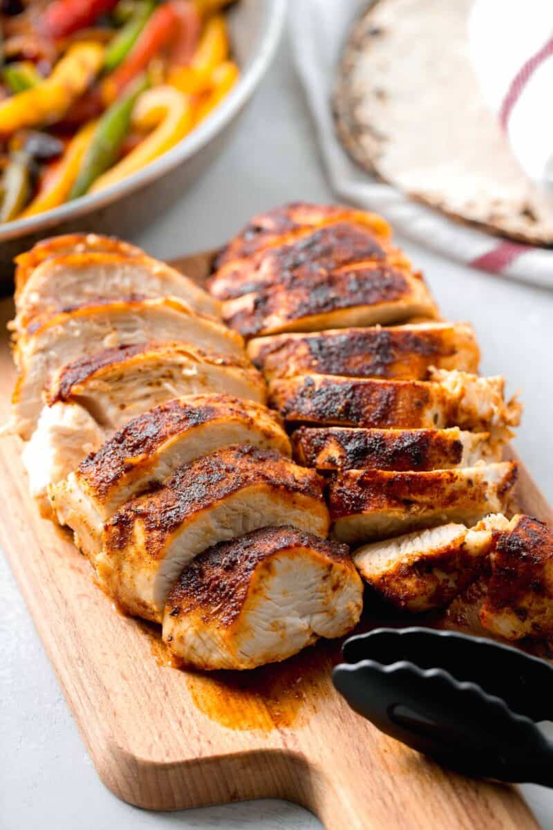 sliced air fryer blackened chicken on a wooden cutting board with black tongs on the cutting board