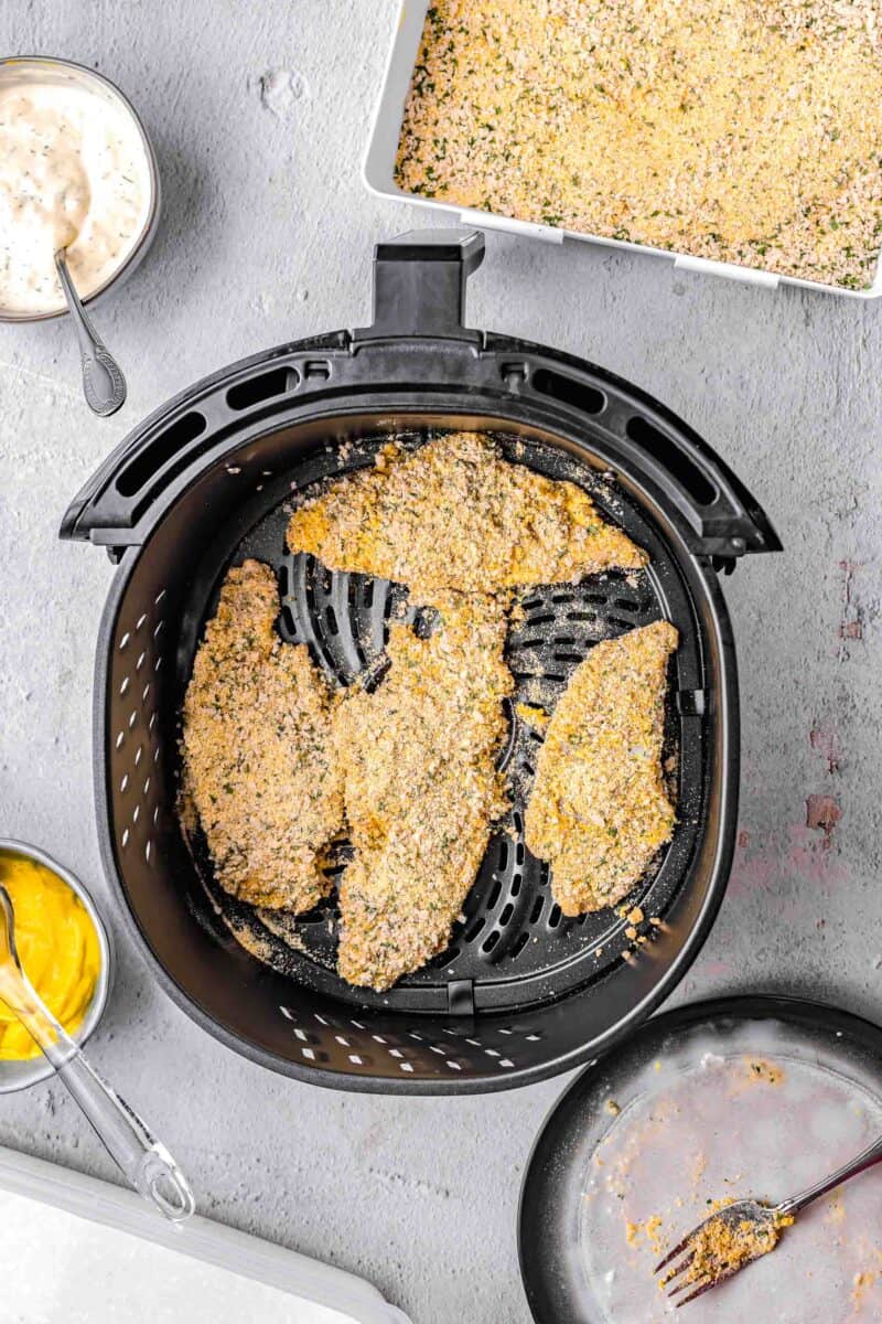 Four pieces of breaded catfish are in the air fryer basket.