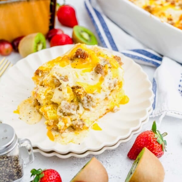 a generous portion of biscuits and gravy casserole on a white scalloped plate with cherries, kiwis, and strawberries in the photo