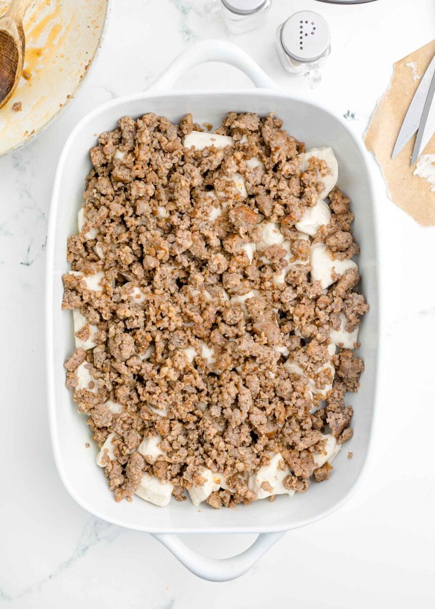 browned sausage pieces on top of quartered biscuits in a white baking dish