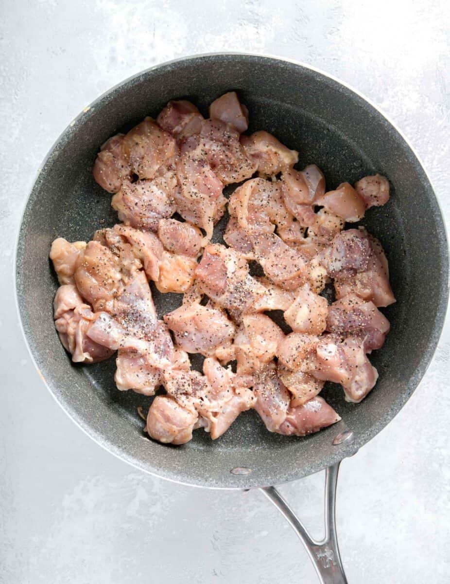 boneless skinless chicken thigh cubes in a grey nonstick skillet with black pepper and salt sprinkled on top