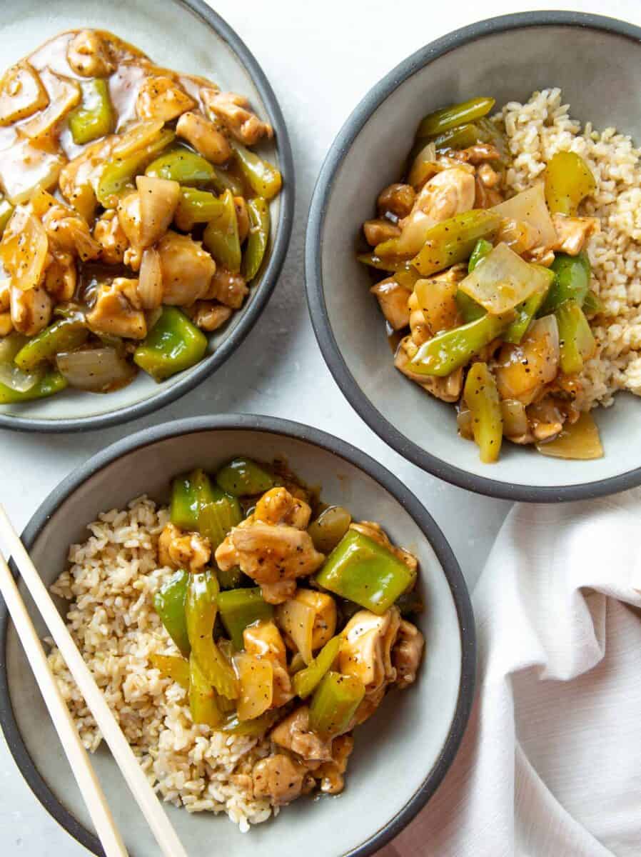 black pepper chicken in grey bowls with brown rice next to plastic chopsticks