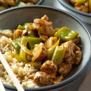 black pepper chicken in a grey bowl with brown rice with chopsticks laying on the bowl