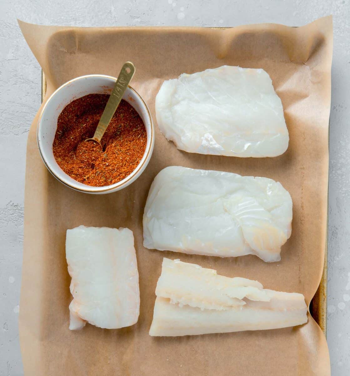 cod filets next to a bowl of blackening seasoning on a parchment lined baking sheet