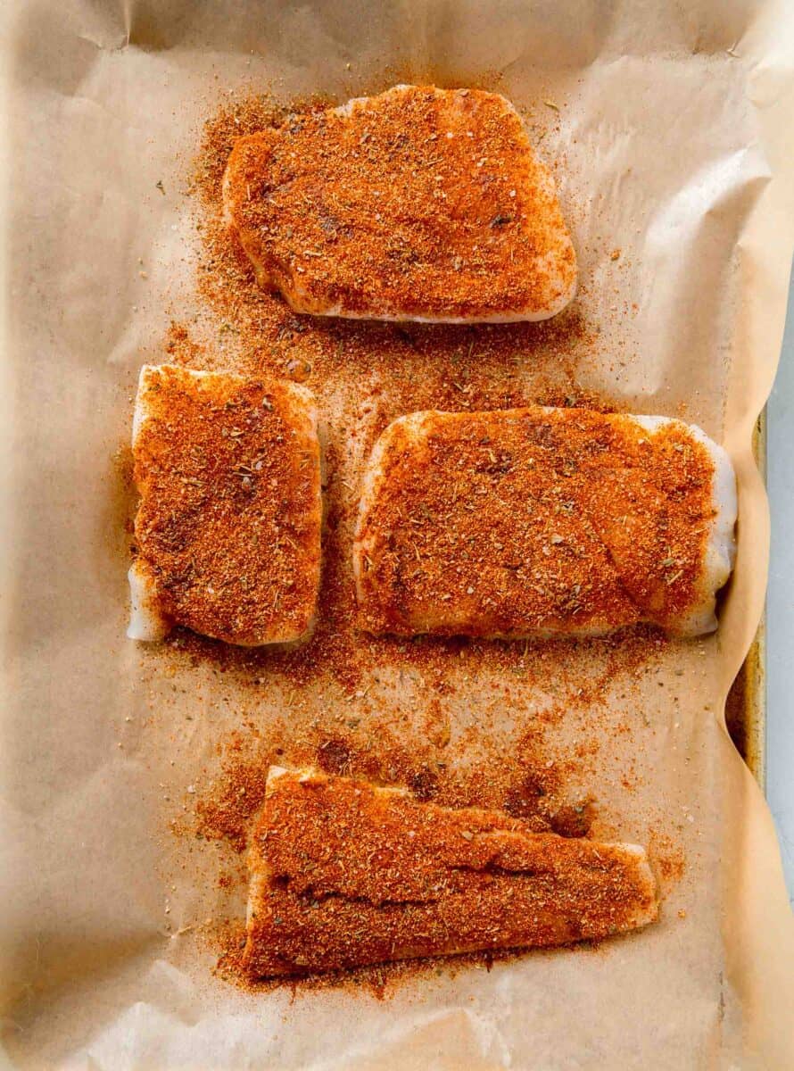 cod filets coated with blackening seasoning on a parchment lined baking sheet