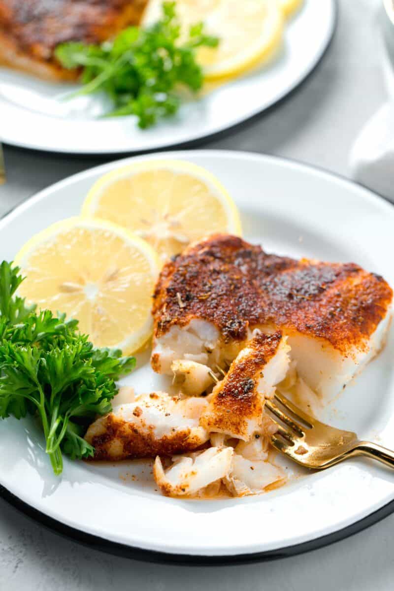 a gold fork breaking apart the tender blackened cod filet on a plate