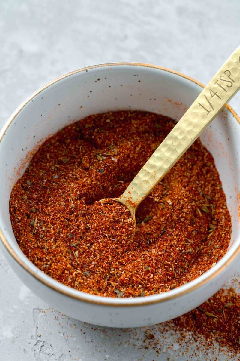 a bowl of blackening seasoning with a gold 1/4 teaspoon spoon inside next to blackening seasoning on the table