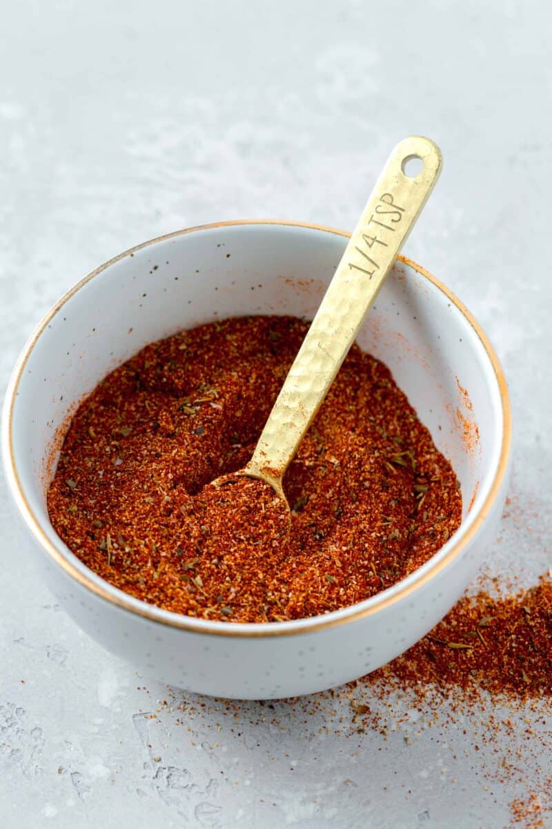 a bowl of blackening seasoning with a gold 1/4 teaspoon spoon inside next to blackening seasoning on the table
