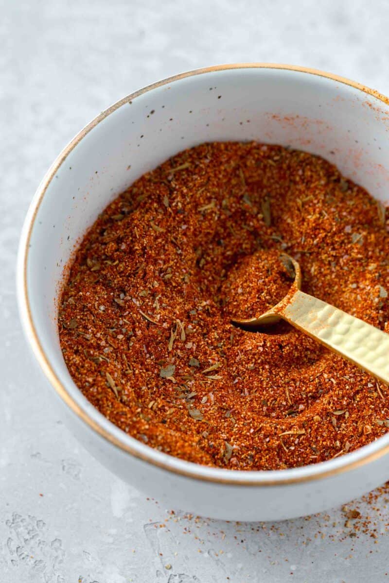 a bowl of blackening seasoning with a gold 1/4 teaspoon spoon inside next to blackening seasoning on the table