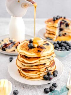 syrup is being drizzled on top of a stack of blueberry pancakes.