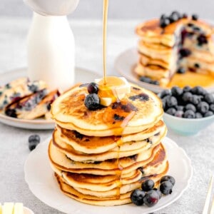 syrup is being drizzled on top of a stack of blueberry pancakes.
