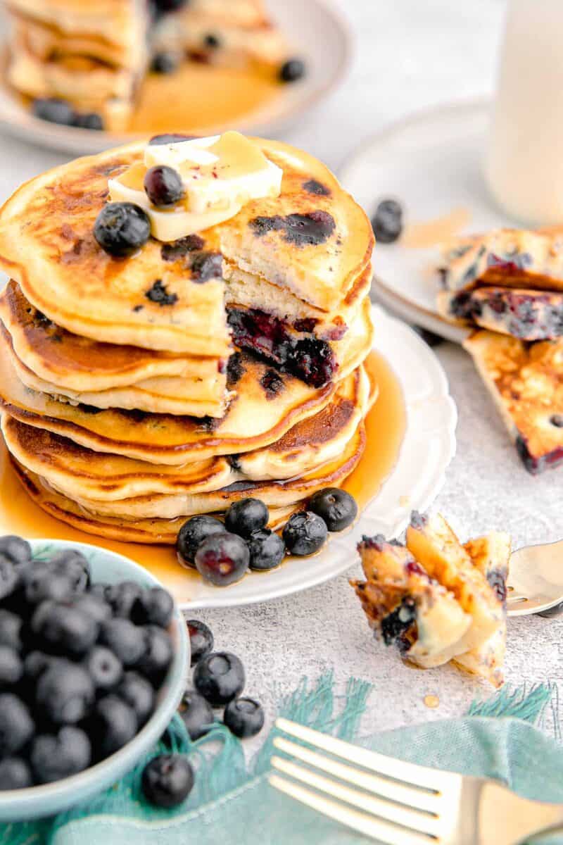 a stack of blueberry pancakes is presented with butter, blueberries, and syrup.