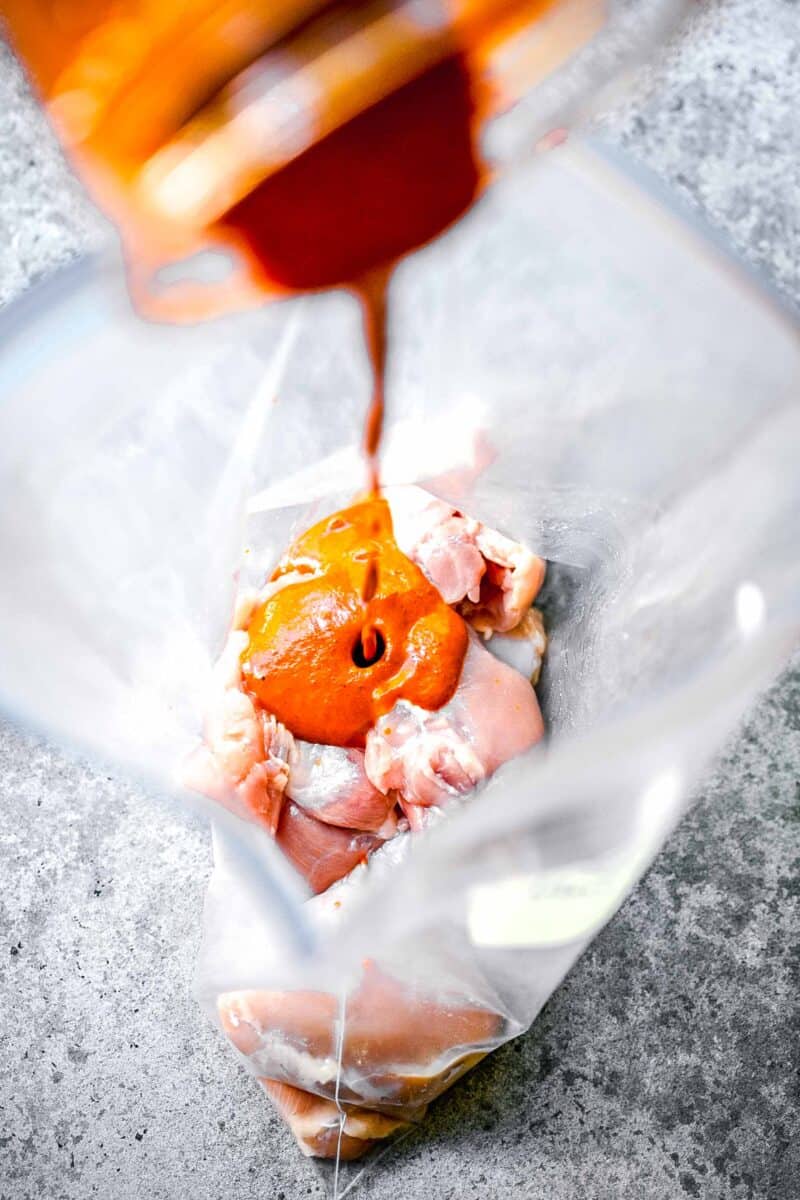 marinade is being poured on top of chicken thighs in a large plastic bag.