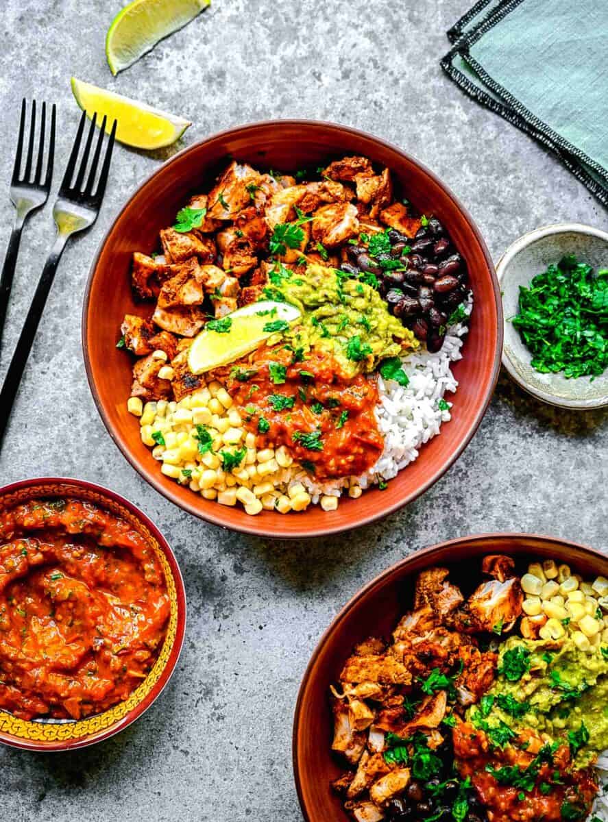 two bowls are filled with toppings, chicken, and rice.