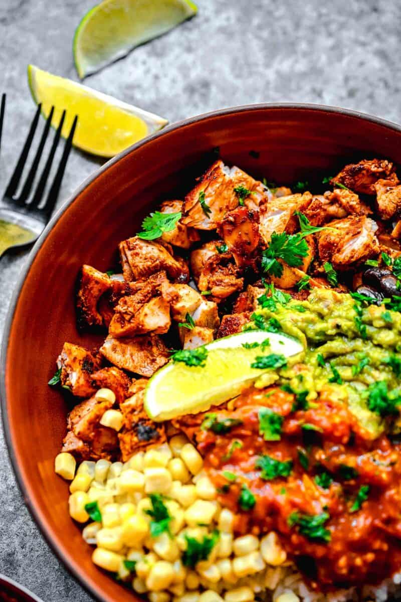 a full chipotle chicken burrito bowl is placed next to a lime wedge and a fork.