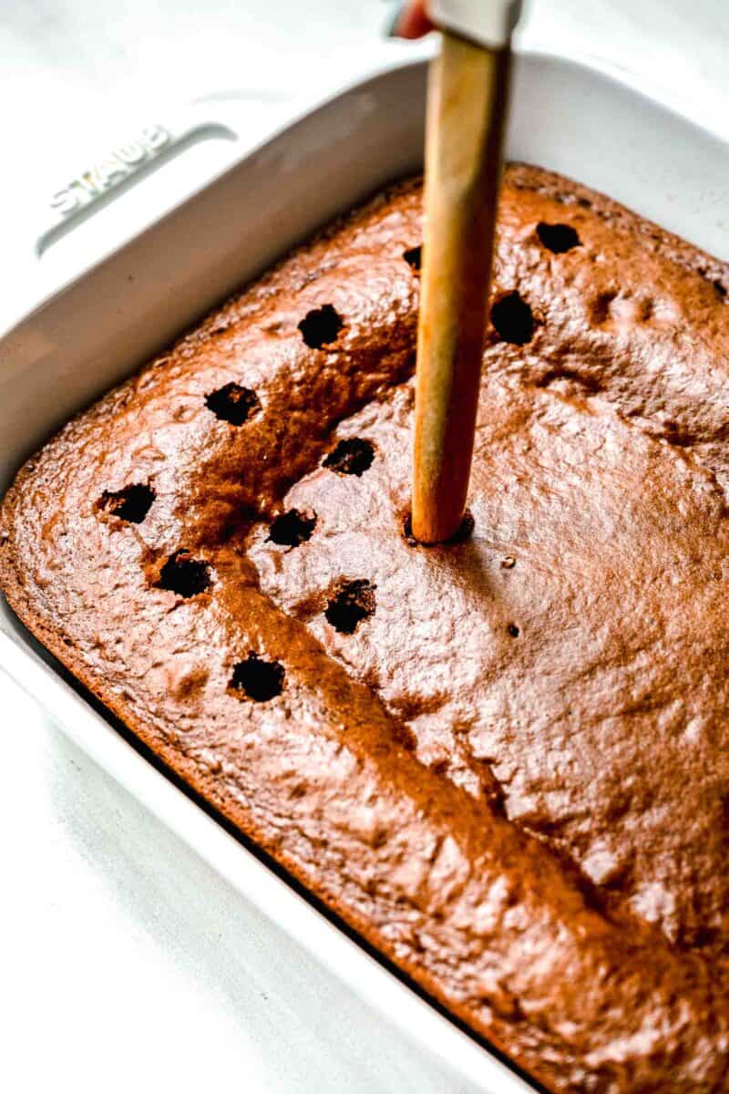 the back of a wooden spoon poking into the baked chocolate cake in the white baking dish