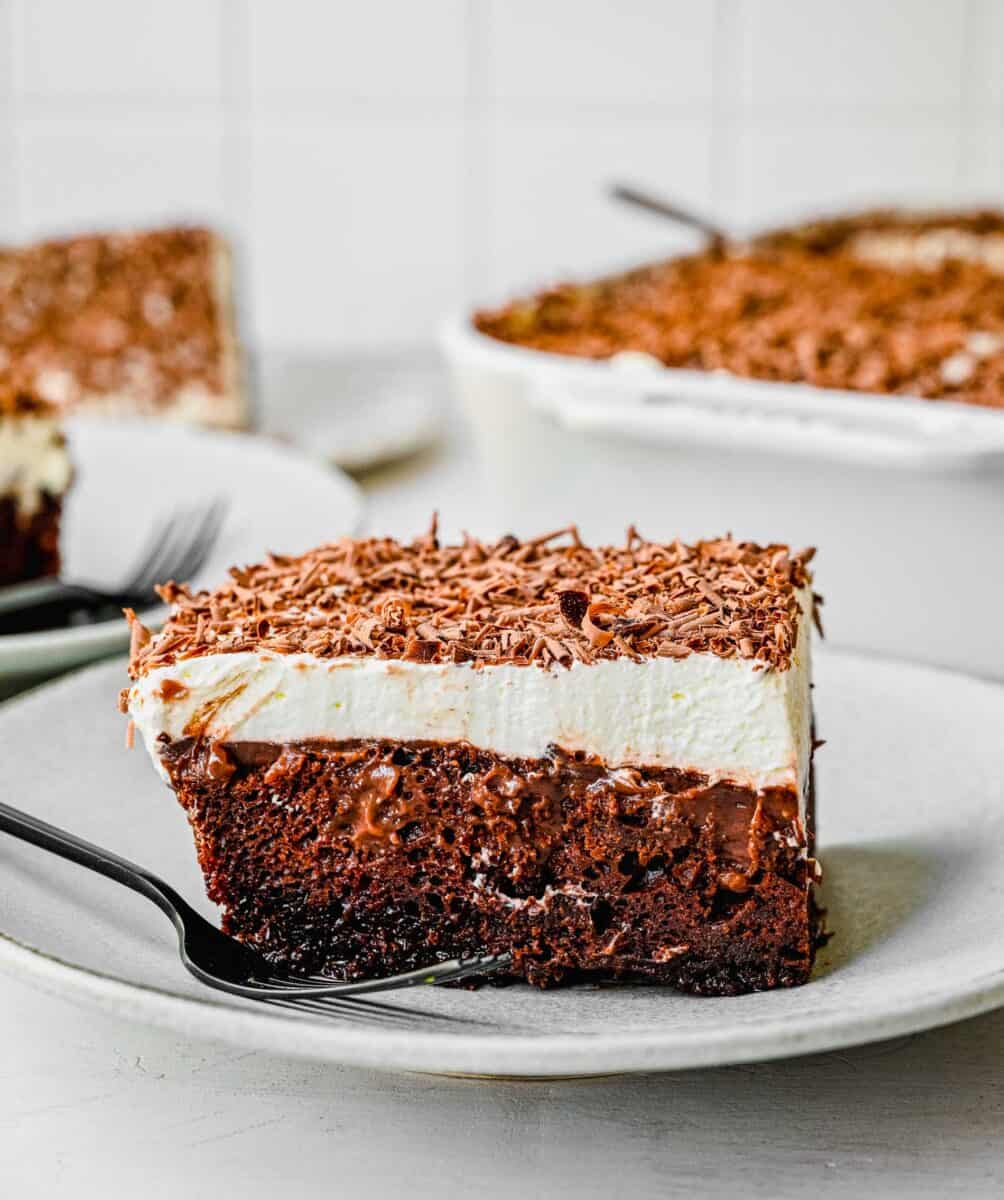 a side view of the chocolate pudding cake. the center is gooey and a black fork can be seen on the white plate with the cake