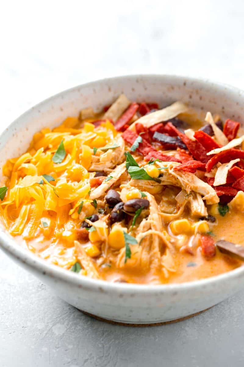 creamy chicken tortilla soup in a ceramic bowl where cheddar cheese, shredded chicken, and tortilla strips can be seen
