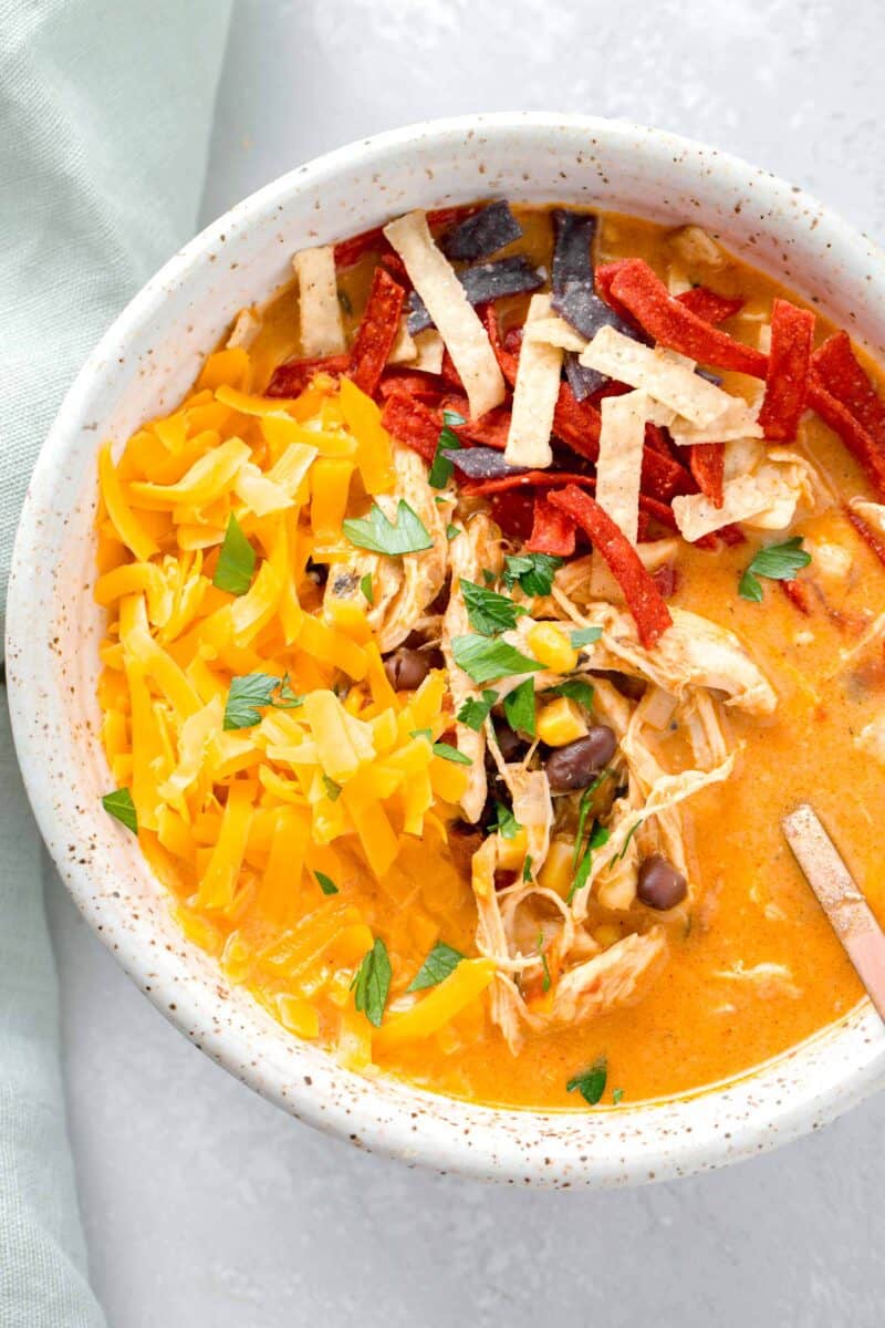 creamy chicken tortilla soup in a bowl with shredded cheese, fresh parsley, and tortilla strips on top