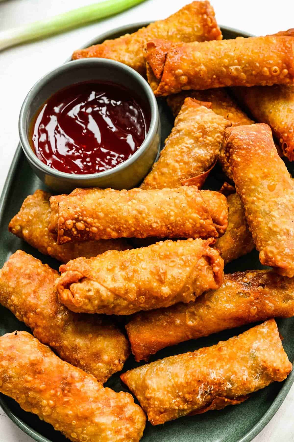 Crispy golden spring rolls on a plate with dipping sauce.