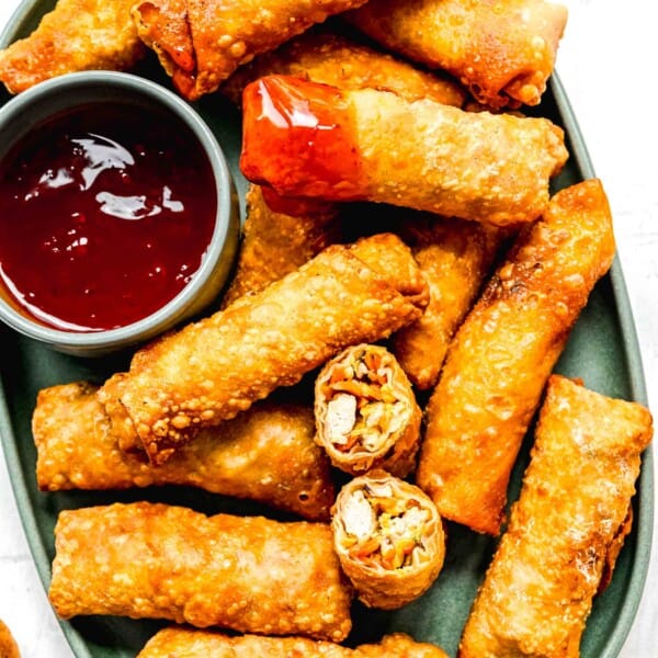 Crispy golden spring rolls on a plate with dipping sauce; one spring roll cut in half and another dipped in sauce.