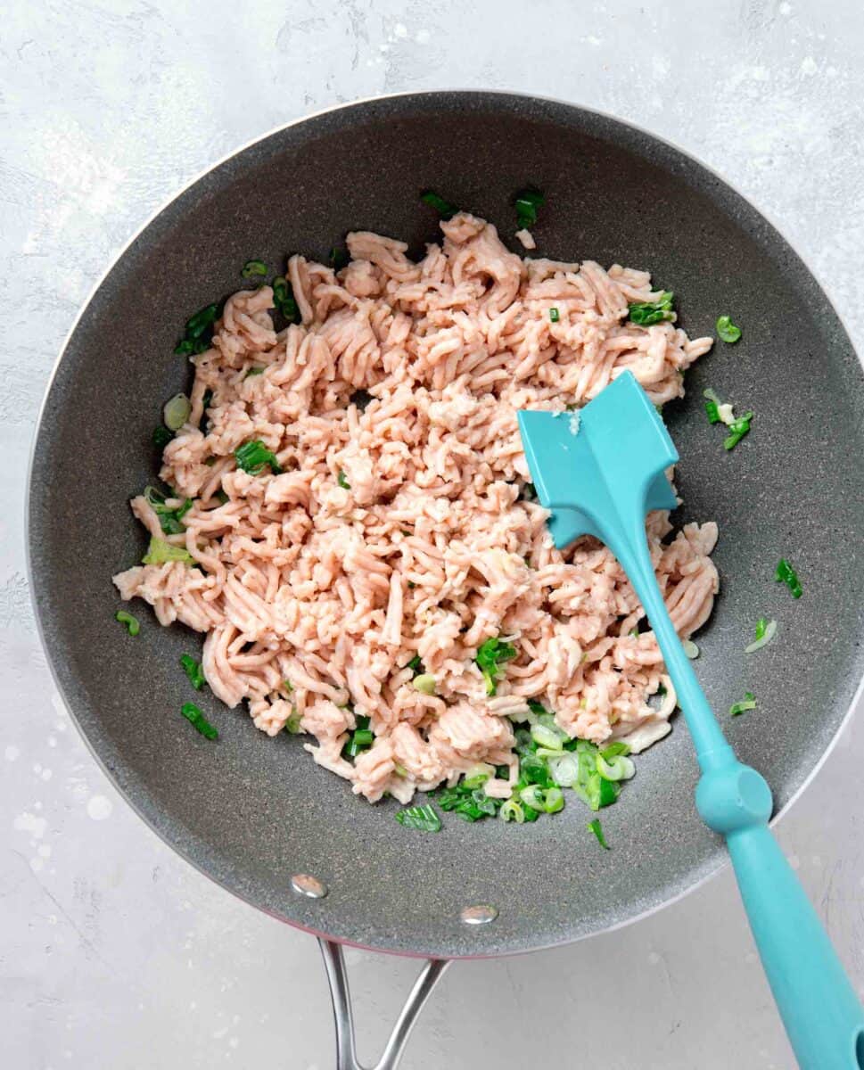 ground chicken and scallions in a grey nonstick skillet with meat masher