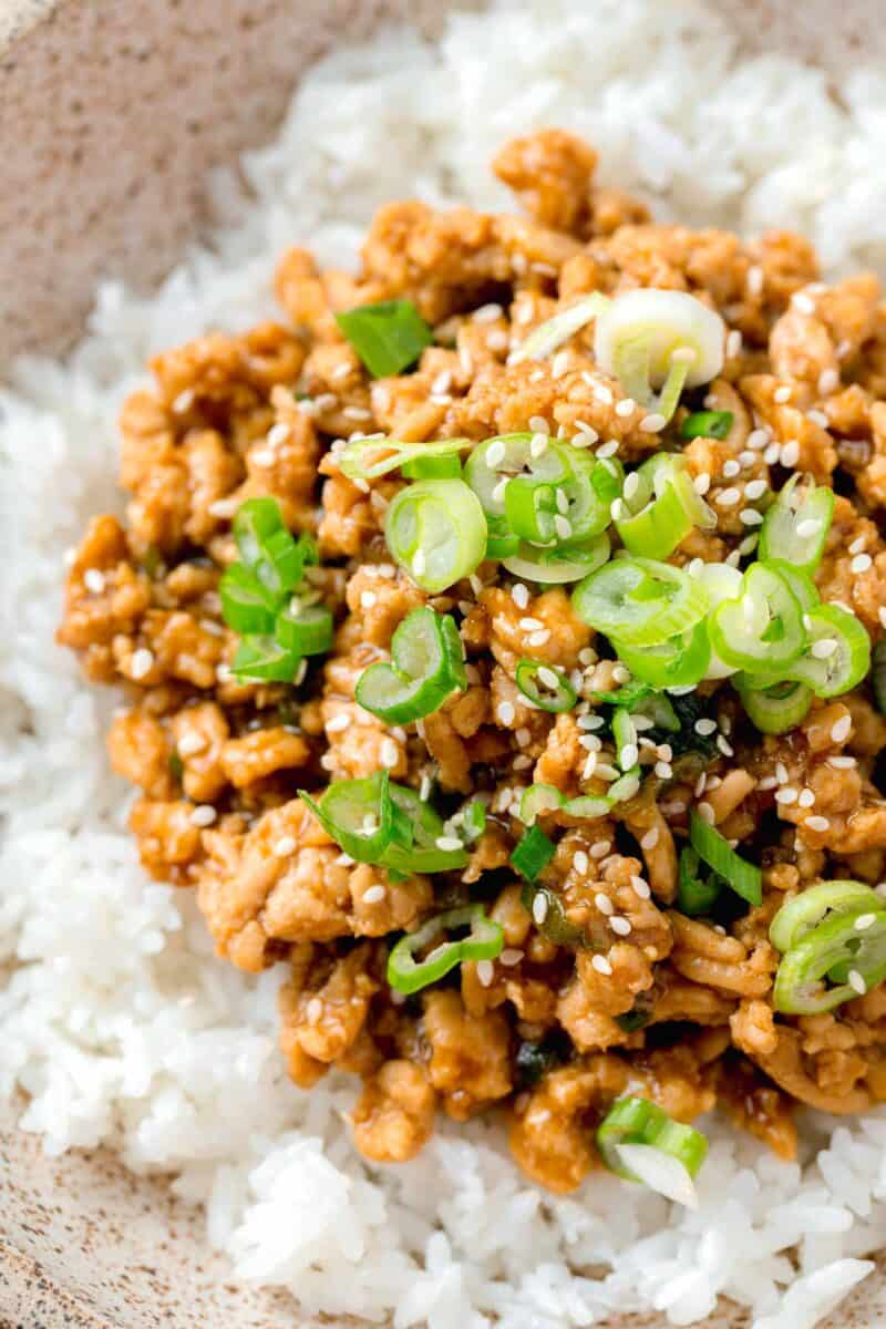ground chicken teriyaki on top of white rice with fresh green scallions and sesame seeds on top