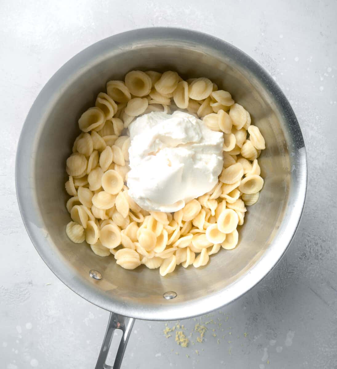 ricotta cheese being added into a stainless steel pot with cooked pasta