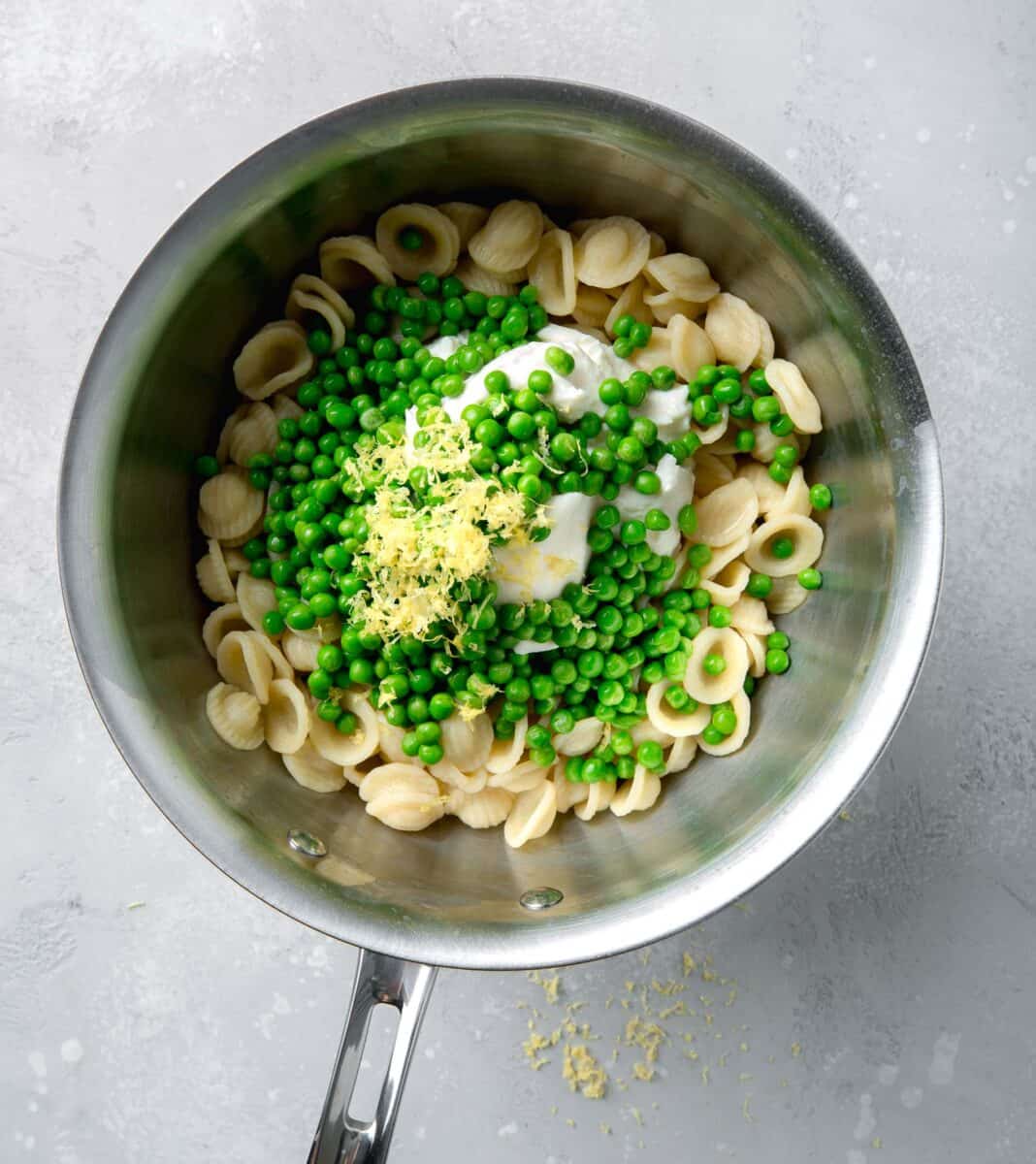 peas and lemon zest added on top of ricotta cheese and cooked pasta in a stainless steel pot