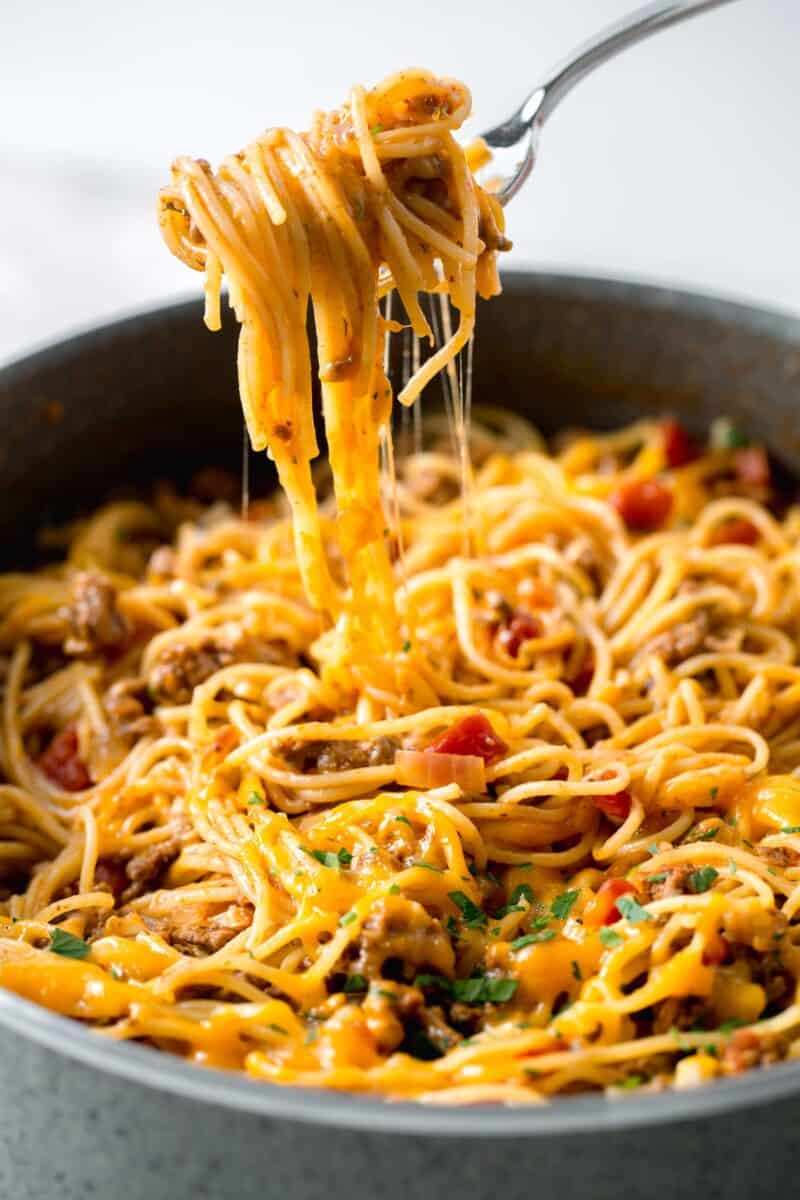 taco spaghetti being pulled out of skillet with a fork and a cheese pull can be seen