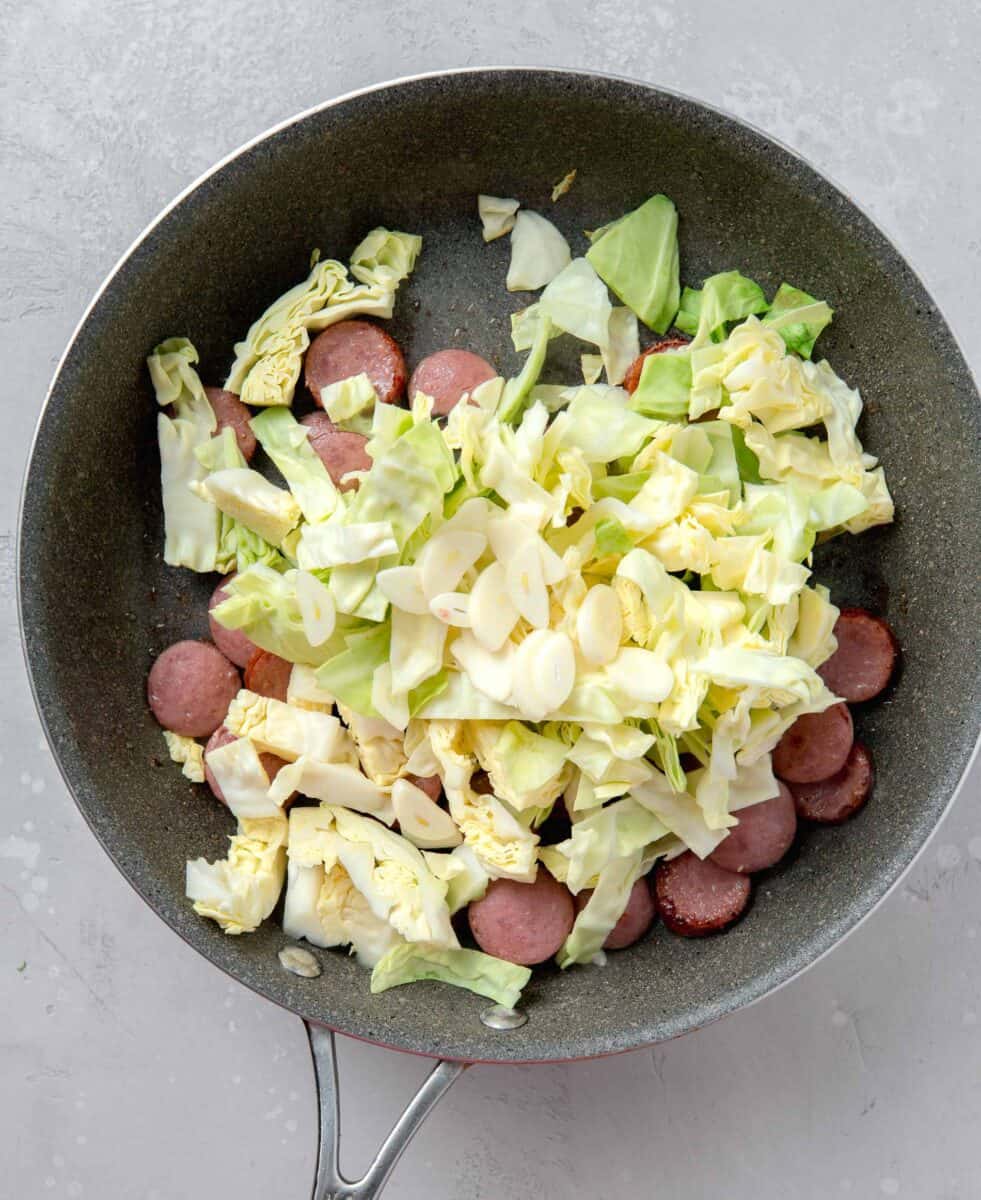 cabbage and sliced garlic added on top of sliced sausage in a nonstick skillet