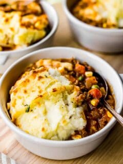 shepherd's pie is placed in a white bowl with a silver spoon.