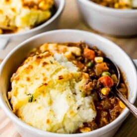 shepherd's pie is placed in a white bowl with a silver spoon.