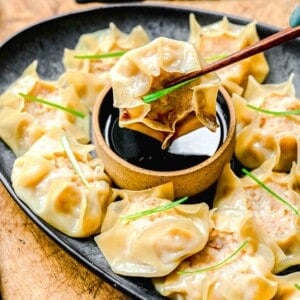 Chopsticks picking up shrimp shumai from a plate with soy sauce.