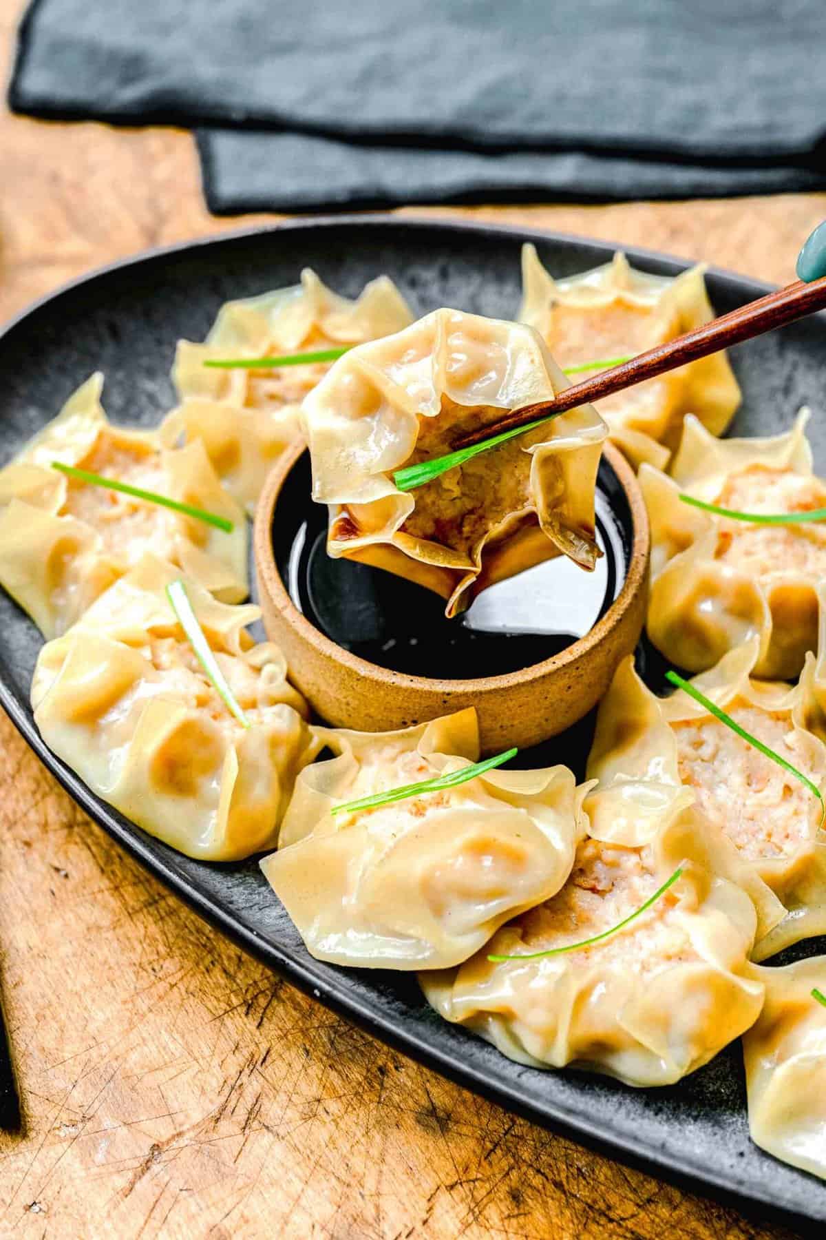 Chopsticks picking up shrimp shumai from a plate with soy sauce.