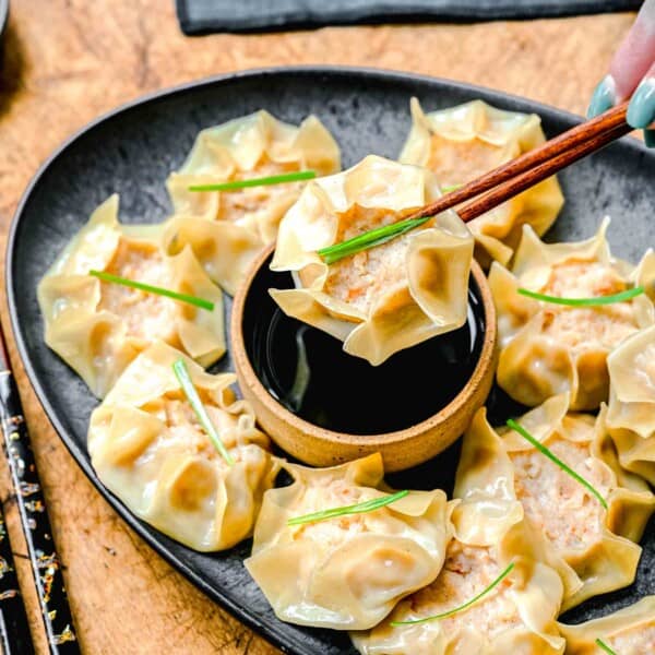 Chopsticks picking up shrimp shumai from a plate with soy sauce.