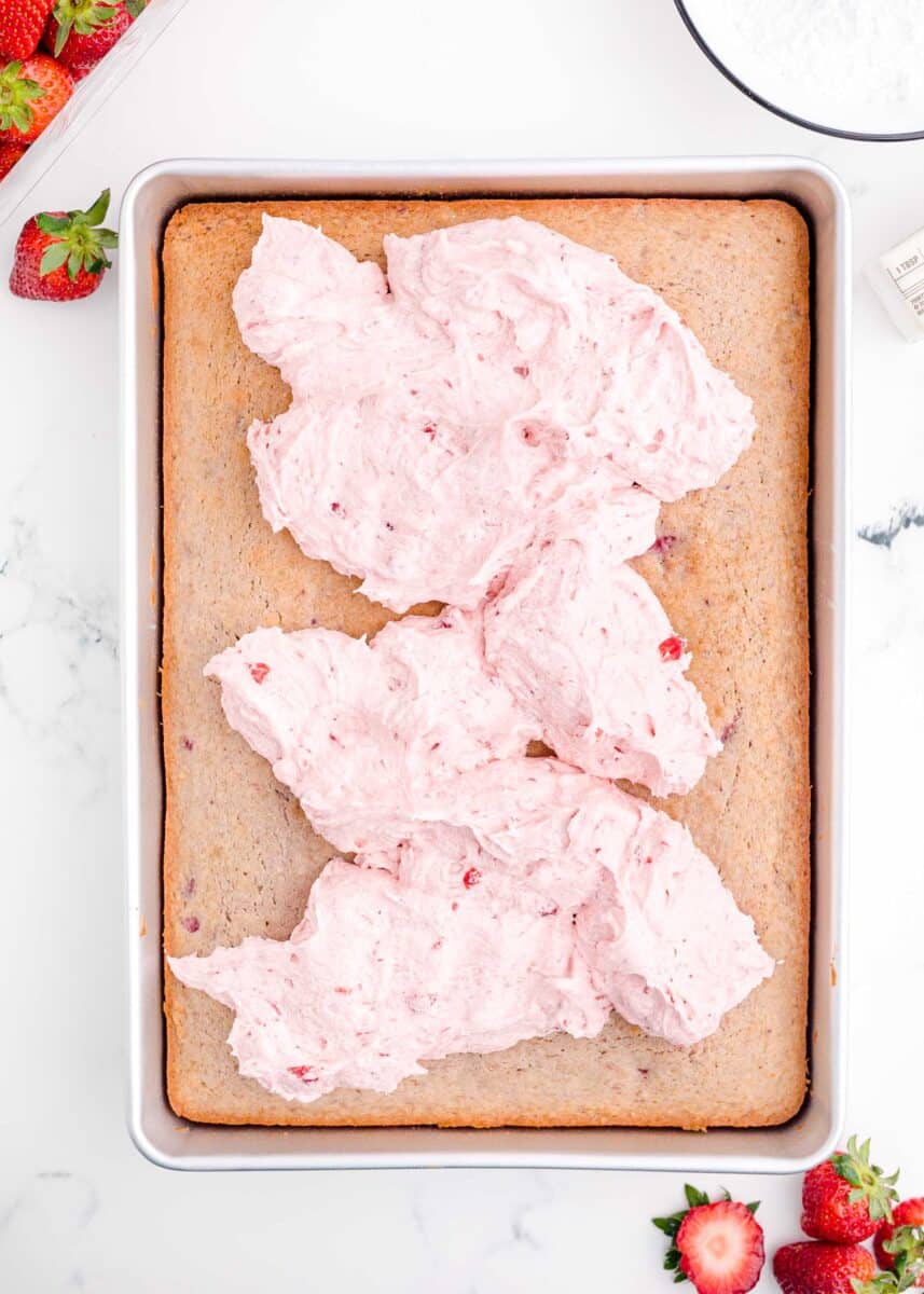 strawberry buttercream dolloped on top of baked strawberry sheet cake in a metal sheet pan