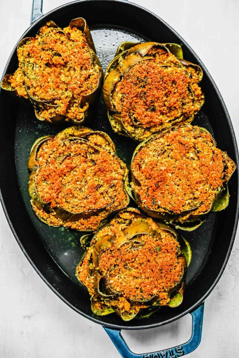baked stuffed artichokes with browned breadcrumb toppings in a cast iron skillet